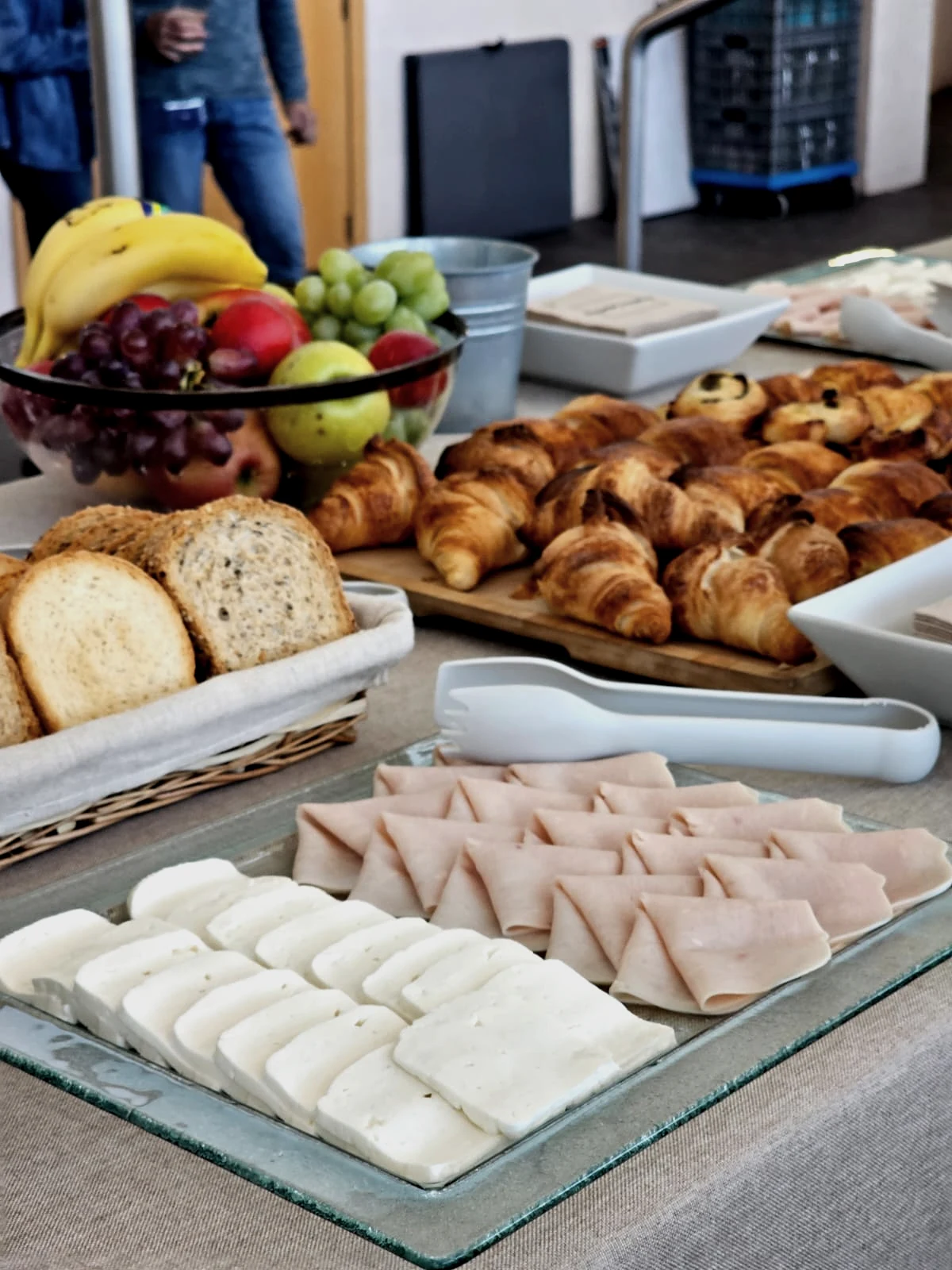 Bandeja de cristal con queso fresco y jamón de pavo, croissants, panes integrales y bowl de fruta