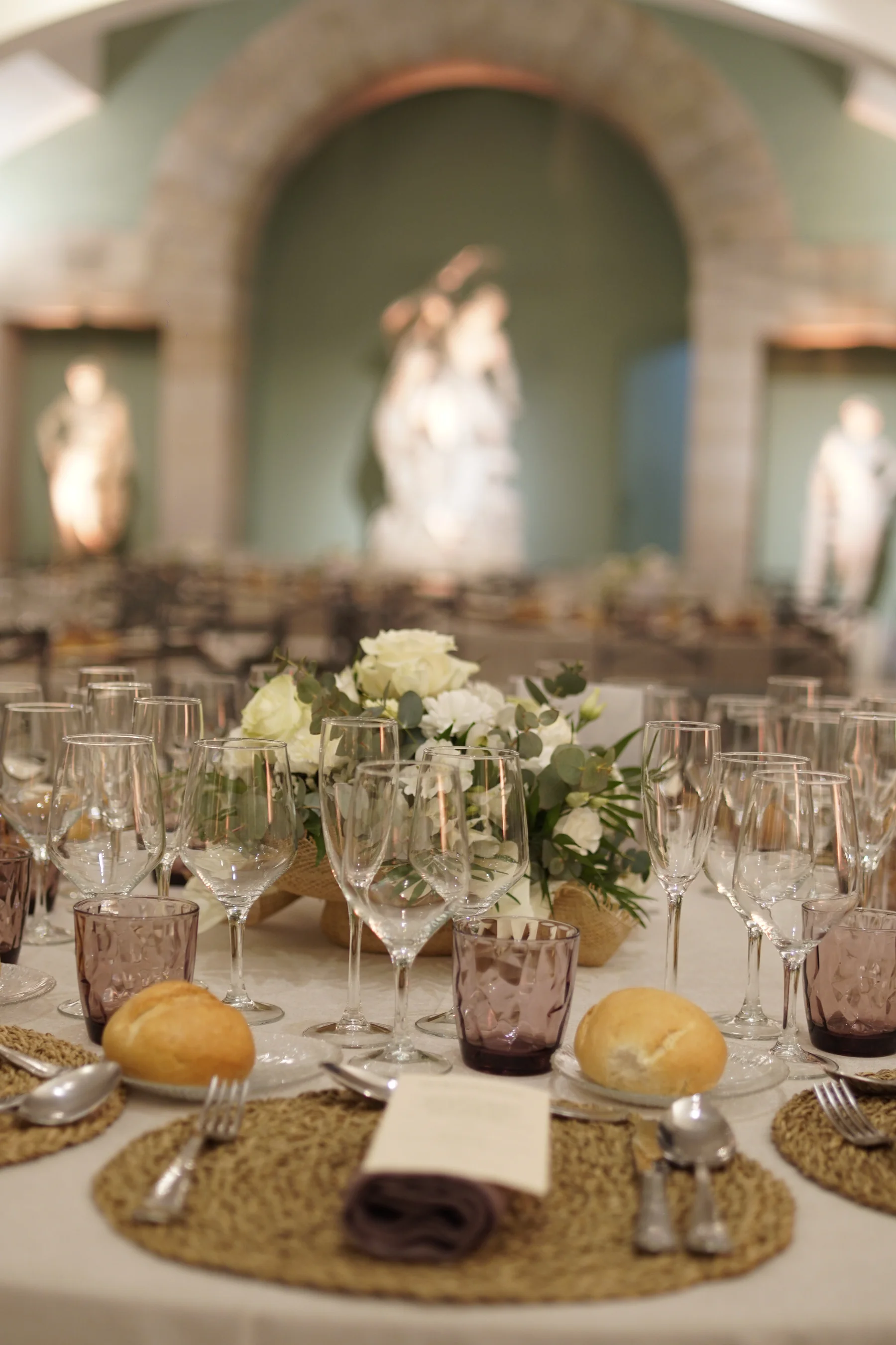 Mesa redonda vestida para banquete de comunión con flores blancas y panecillos